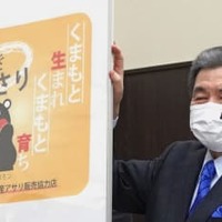 販売店で熊本県産アサリの小売り用パックなどに貼られるシールの図案を掲げる蒲島郁夫知事＝12日午後、熊本市