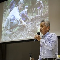 木村汐凪さんの捜索時の写真を背に講演する具志堅隆松さん＝4日午後、福島県大熊町