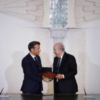 27日、アルジェで握手するアルジェリアのテブン大統領（右）とフランスのマクロン大統領（AP＝共同）