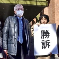 「勝訴」と書かれた紙を掲げる弁護士と原告の奥田恭正さん＝18日午後、名古屋地裁前