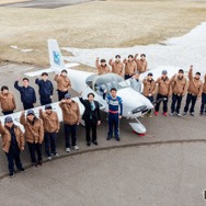軽量飛行機を囲んで記念撮影するテクノアカデミーの学生と室屋義秀選手