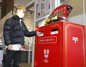 正月飾りが付けられたポストに年賀状を投函する人＝15日午前、東京中央郵便局