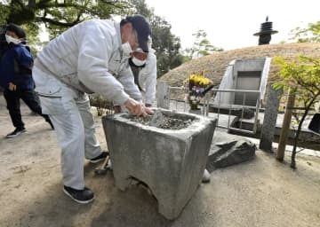 セメントのようなもので埋められた鉢の修復作業。奥は原爆供養塔＝20日午前、広島市の平和記念公園