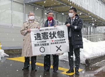 衆院選の「1票の格差」訴訟の判決を受け、仙台高裁秋田支部前で「違憲状態」と書かれた紙を掲げる弁護士＝15日午後