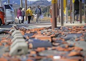福島県相馬市で給水に並ぶ人たち。手前には瓦が崩落したままだった＝19日午前
