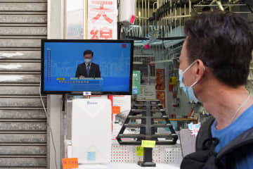 李家超氏による行政長官選挙出馬会見のテレビ中継を見る人＝9日、香港（ロイター＝共同）