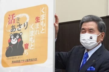 販売店で熊本県産アサリの小売り用パックなどに貼られるシールの図案を掲げる蒲島郁夫知事＝12日午後、熊本市