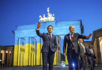 ウクライナ国旗の色に照らされたブランデンブルク門の前で撮影に応じるフランスのマクロン大統領（左）とドイツのショルツ首相＝9日、ベルリン（AP＝共同）