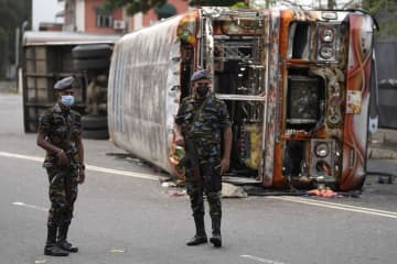 10日、スリランカ・コロンボで、燃えたバスの前に立つ兵士（AP＝共同）