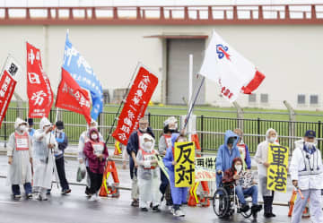 米軍那覇港湾施設の浦添市への移設に反対し、キャンプ・キンザー（奥）の前をデモ行進する人たち＝13日午後、沖縄県浦添市