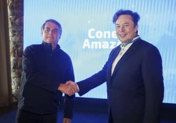 米電気自動車テスラのイーロン・マスクCEO（右）と握手するブラジルのボルソナロ大統領＝20日、ブラジル・ポルトフェリス（ブラジル通信省提供、AP＝共同）