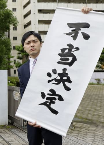 鹿児島地裁が「大崎事件」の再審開始を認めない決定をしたことを受け、「不当決定」と書かれた紙を掲げる弁護士＝22日午前、鹿児島市