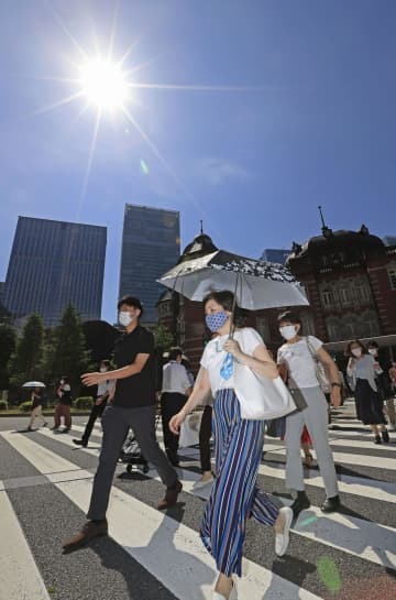厳しい暑さの中、マスク姿で歩く人たち＝27日午前、JR東京駅前