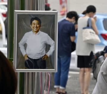 献花台に飾られた安倍元首相の写真。奥は銃撃された現場近くで手を合わせる人たち＝7月15日、奈良市
