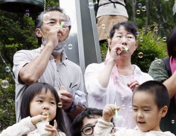 「御巣鷹の尾根」にある「昇魂之碑」の前でシャボン玉を飛ばす早坂由里子さん（奥右）。同左は夫の満さん＝12日午前、群馬県上野村