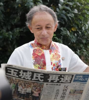 沖縄県知事選から一夜明け、自身の再選を報じる新聞を手にする玉城デニー氏＝12日午前、那覇市