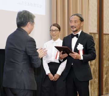 地域貢献大賞を受賞し、日本新聞協会の丸山昌宏会長（左）から表彰される長崎新聞青方販売センターの芳賀良介所長と妻佳美さん＝17日午後、東京都内