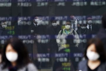 13日、東京都内の株価ボードに反射して写る、マスク姿の人たち（AP＝共同）