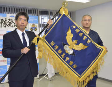 沖縄県警の「国境離島警備隊」発足式で宮沢忠孝本部長（左）から小林雅哉隊長に授与された隊旗＝1日午後、沖縄県警本部